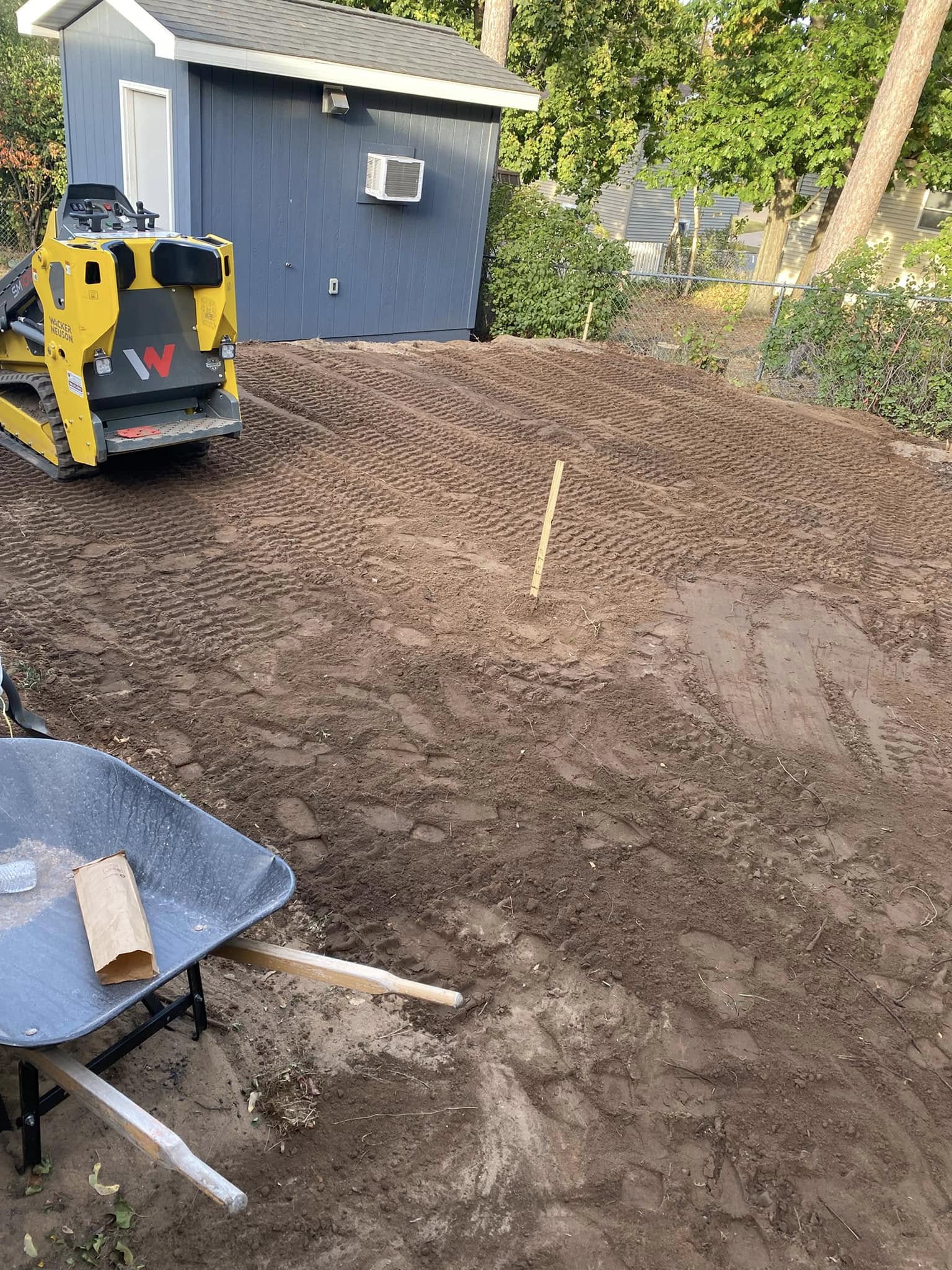 Cornerstone_8 Yellow skid steer grading dirt behind a blue shed.