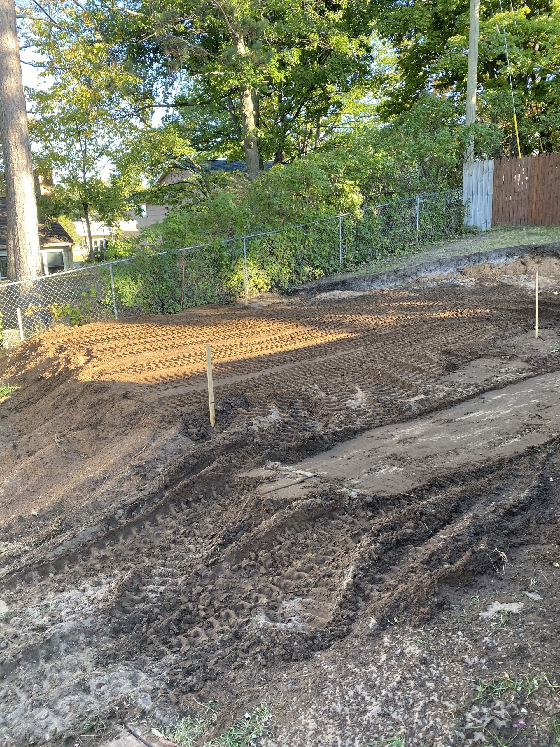 Freshly graded dirt yard with machine tracks and wooden stakes.